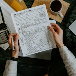 Manos revisando documentos fiscales con una calculadora y un portatil sobre la mesa