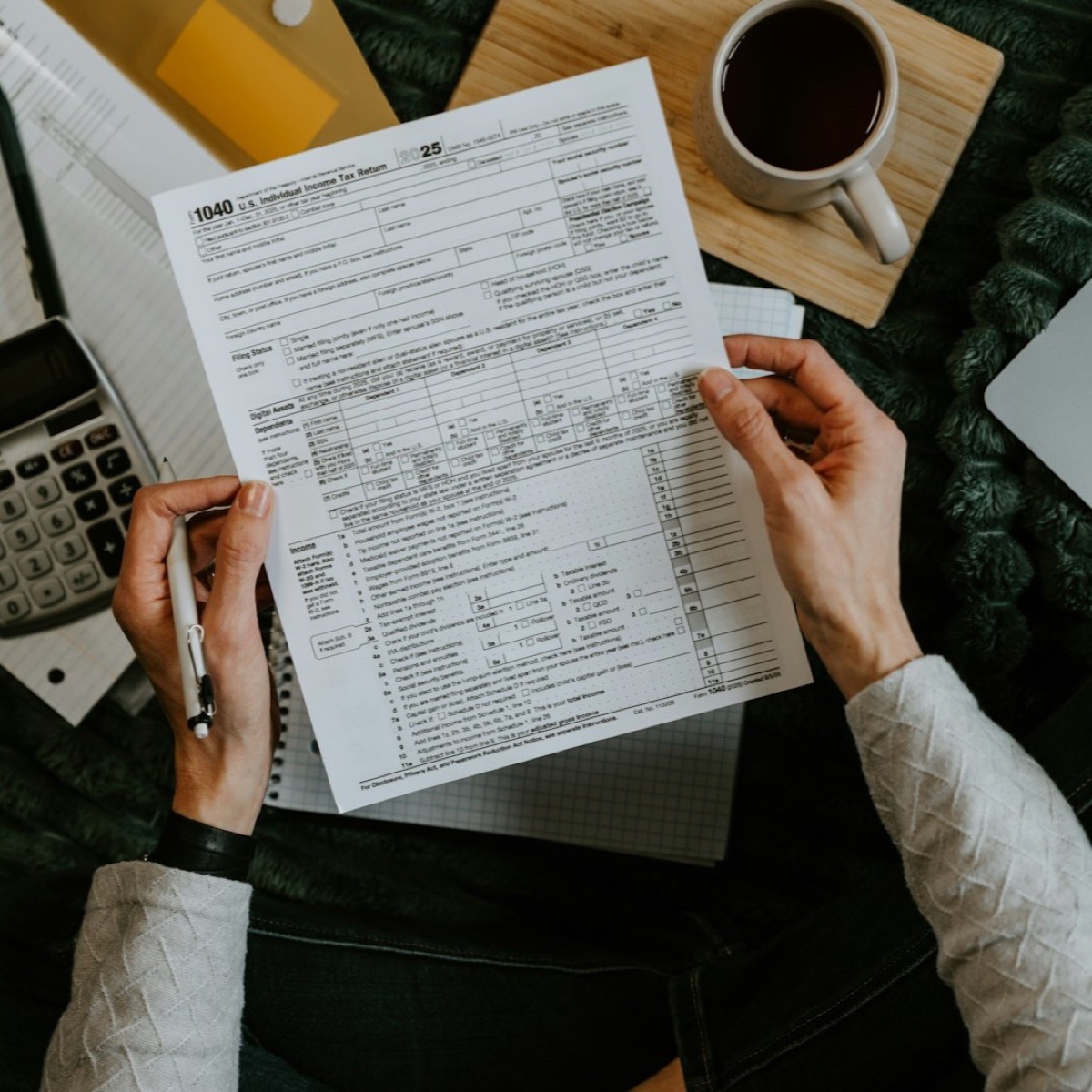 Manos revisando documentos fiscales con una calculadora y un portatil sobre la mesa